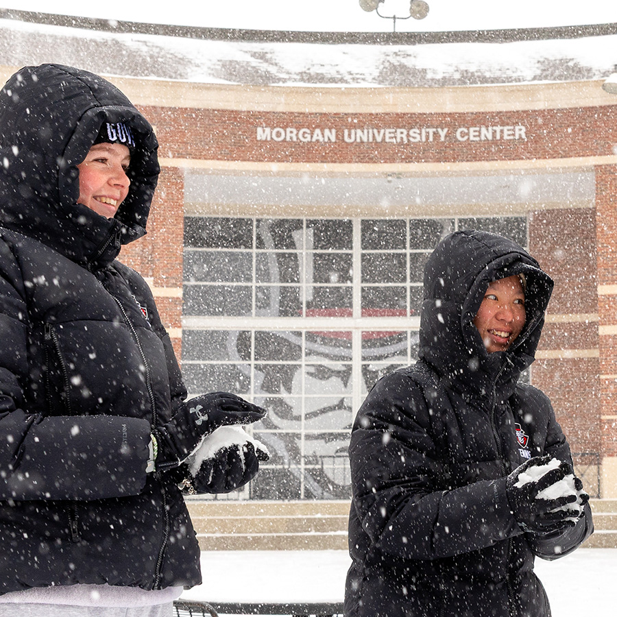 A group of three students making snowballs in front of the Morgan University Center.