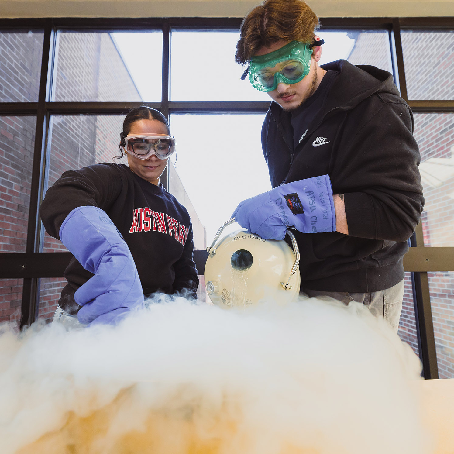 Two students using liquid nitrogen during a soap making demonstration in the College of STEM creating a large amount of foggy vapor.