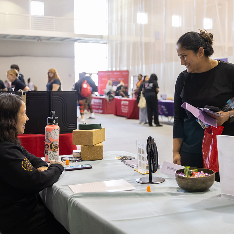 A room full of tables/booths with a woman standing in front of a table that another woman is sitting at and smiling to each other.