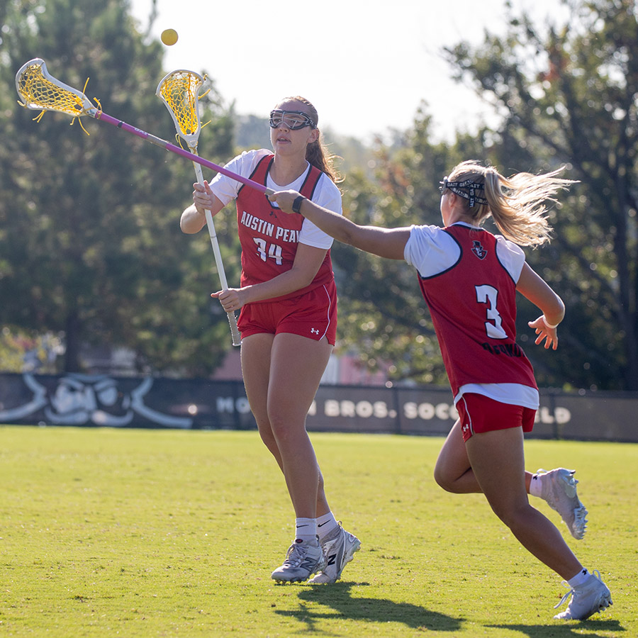 Two women's lacrosse players attempting to catch the ball with outstretched rackets.