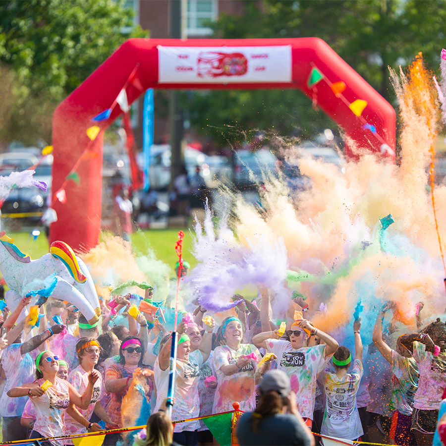 A crowd of people in front of a blow-up race arch getting covered in plumes of colorful powder.