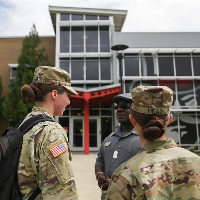 Three individuals, two in military uniforms and one in a gray shirt, converse outside of the APSU Ft. Campbell building.