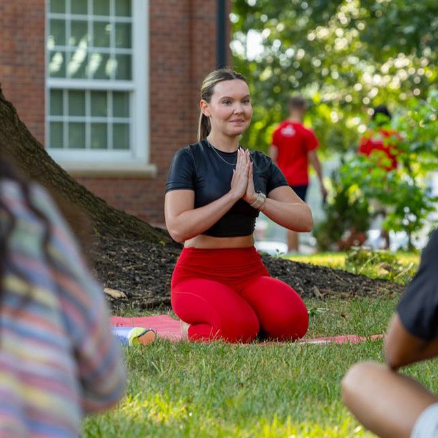 Yoga instructor sitting in a prayer hands pose in front of class-goers.