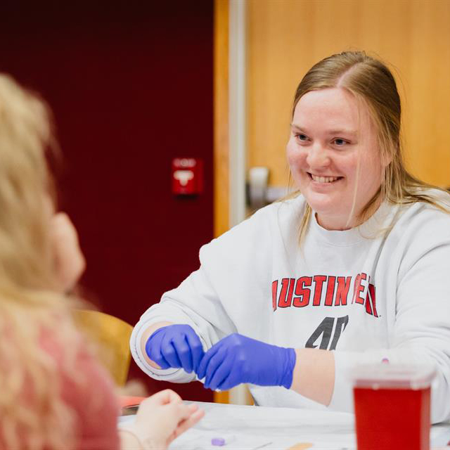 Nursing student wearing latex gloves getting ready to prick a student's finger for a blood test.