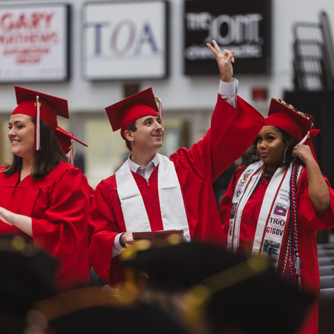 Student waving to their family in the crowd after receiving their diploma at graduation.
