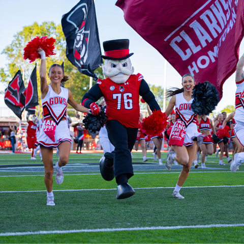 The gov running on football field with cheerleaders