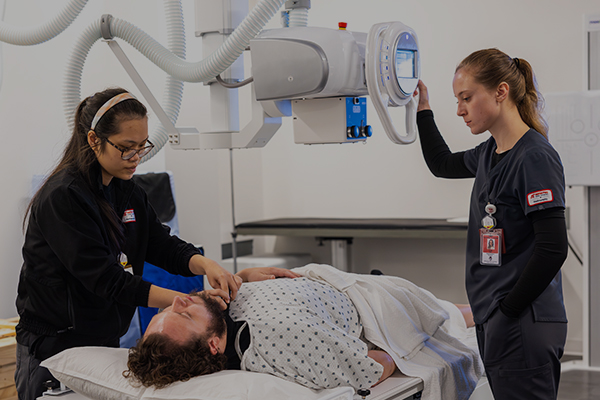 Two rad tech students readying a patient on the table for imaging.