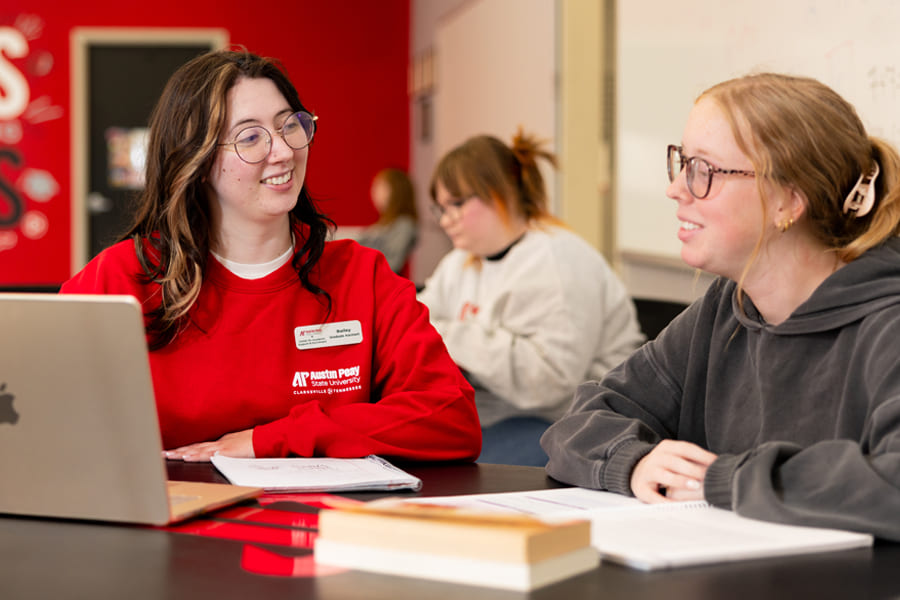 Two students studying together with a laptop and books sitting in front of them.