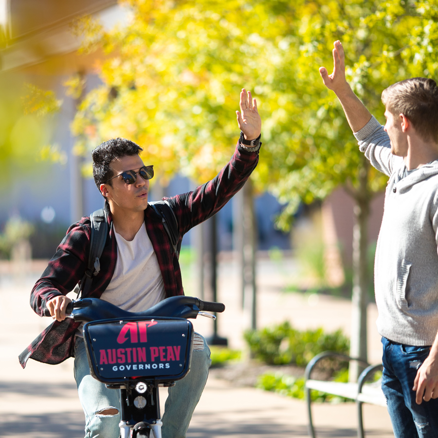 Student riding a bike while giving another student a high five