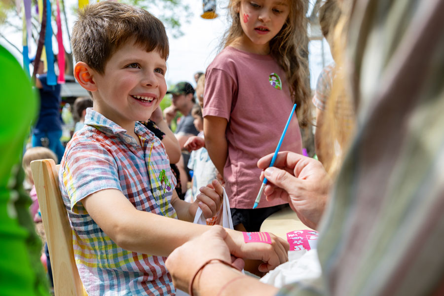 Child smiling as their hand get painted at a festival.