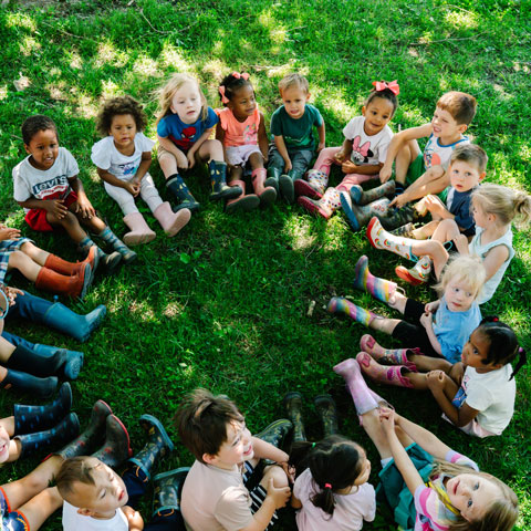 Aerial shot of children sitting in a circle outside on the grass.