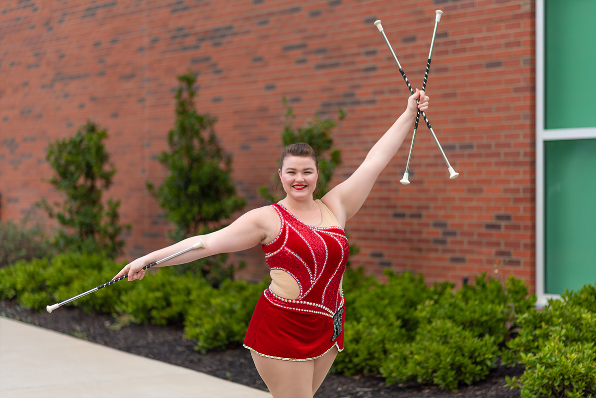 Izzy Melvin poses in front of Art and Design building with twirling batons