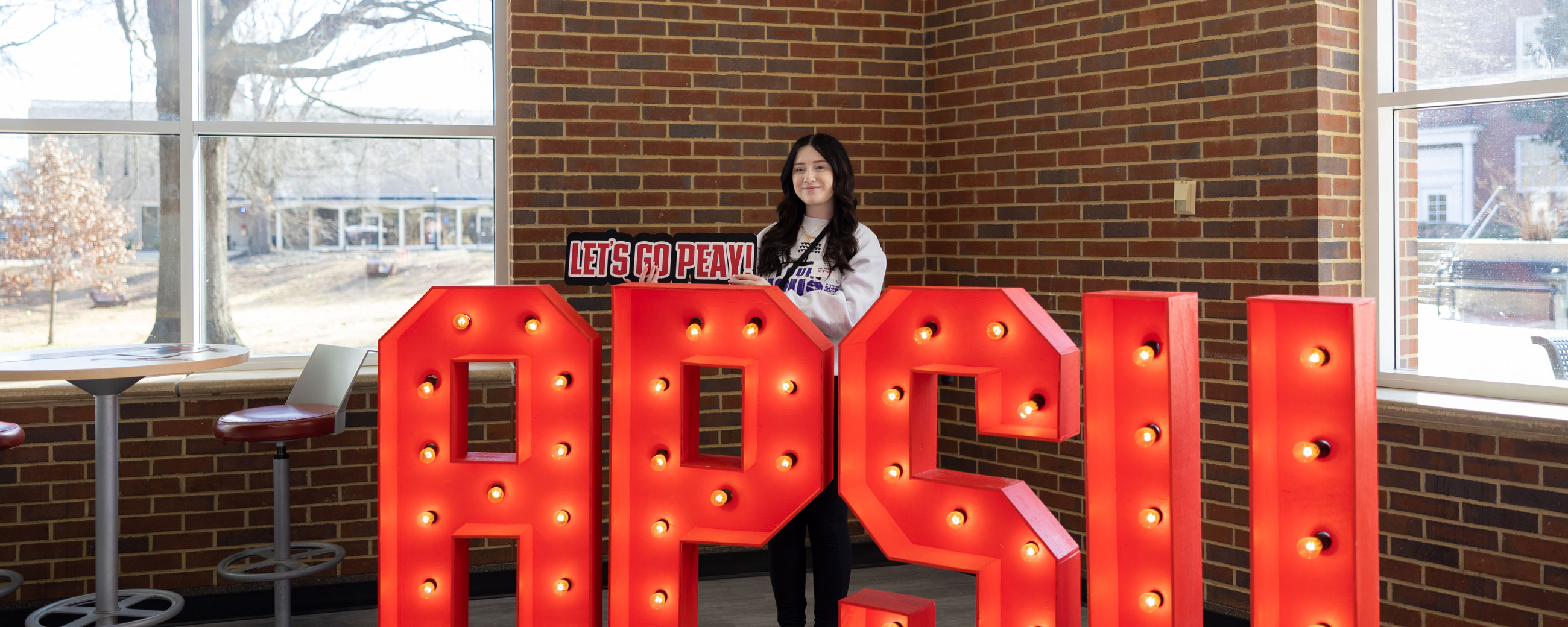 Student standing behind a light up sign that spells APSU