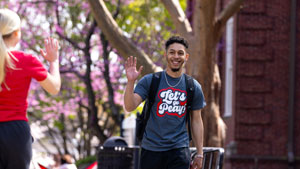 Students waving to each other as they pass on campus. 