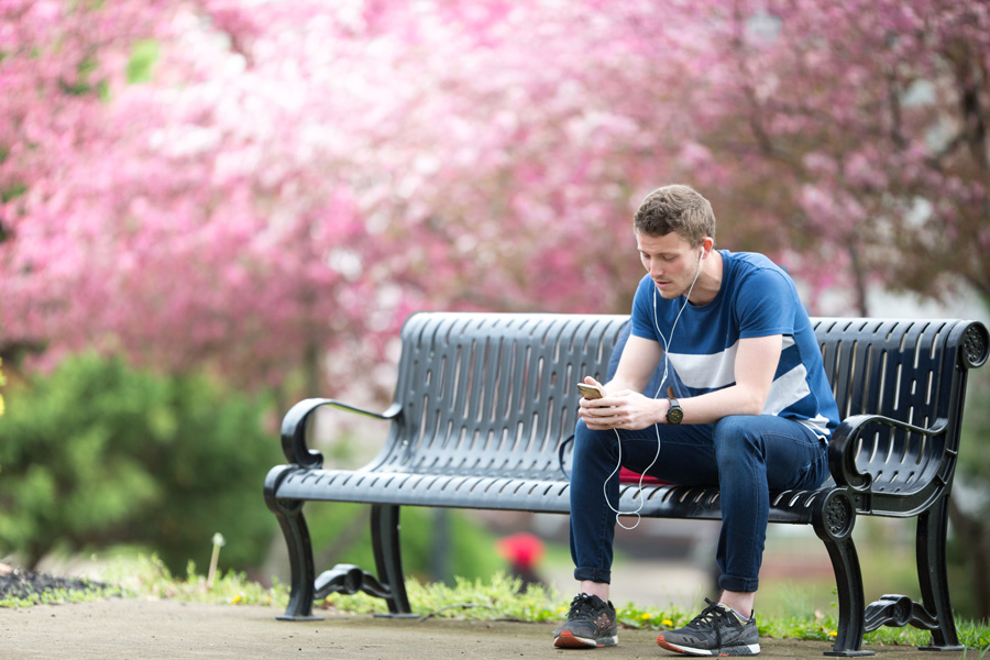 Student sitting on a bench outside listening to music