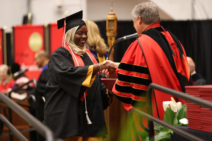 Student shaking hands with the University President while receiving their diploma