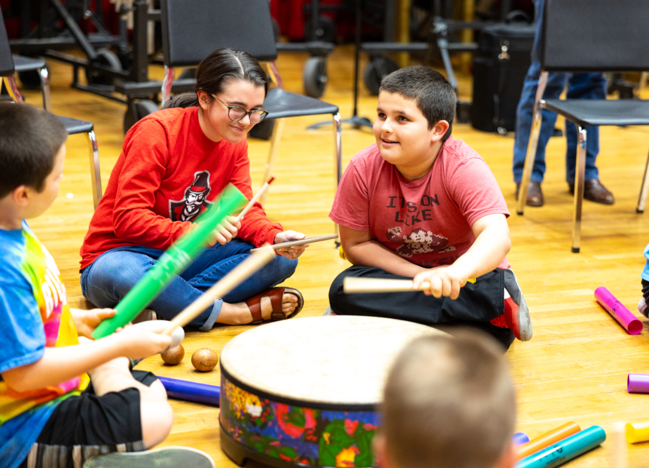 An APSU student sits on the ground and plays drums with several children.
