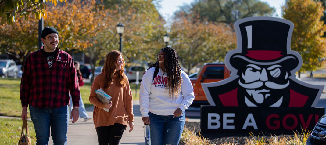 Students walking on campus past the Be A Gov statue.